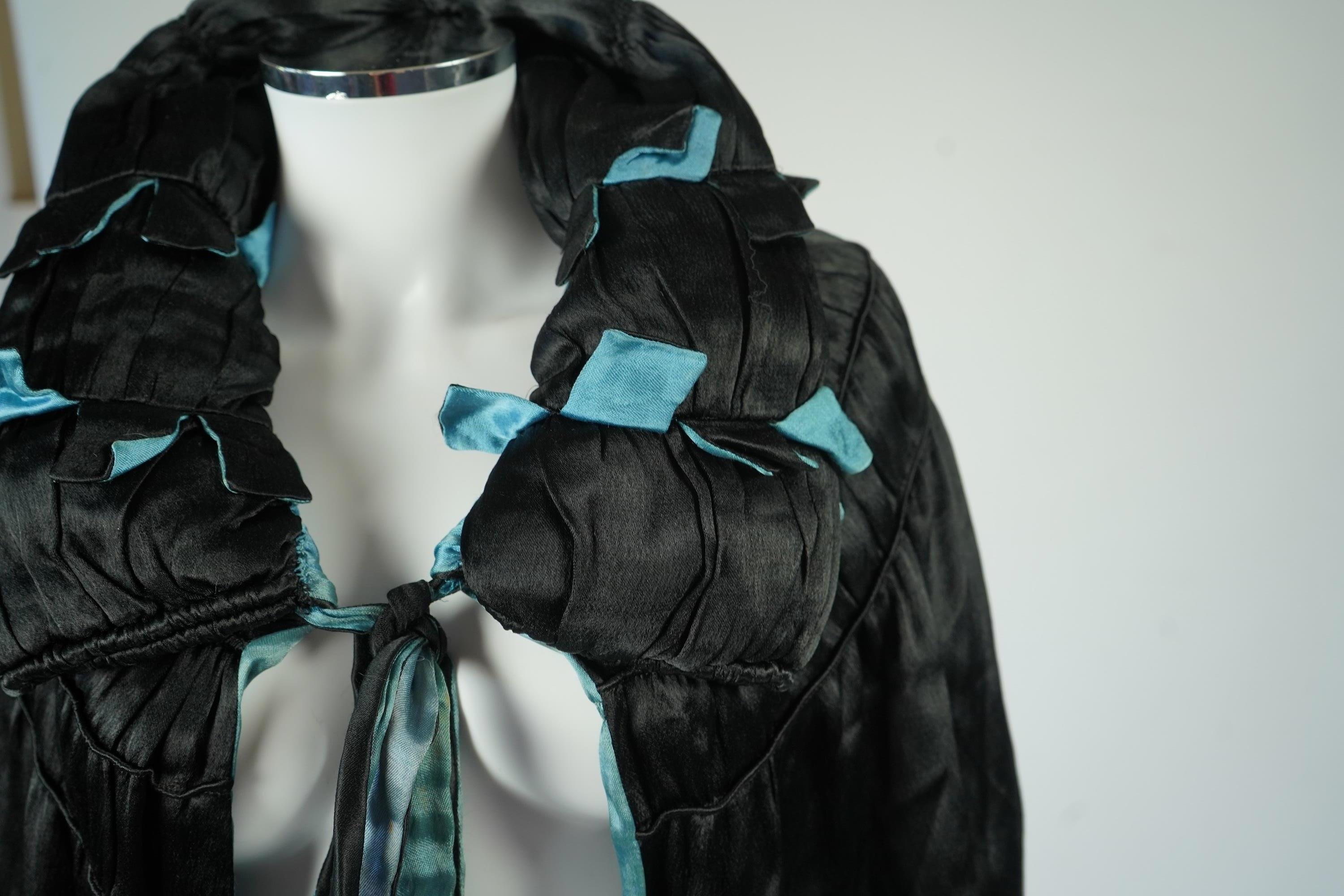 A 1920's ladies blue lined, black silk opera cape. Designed with a rushed ornate collar and scalloped and fringed lower edge. 95cm long fron neck to base. Condition - stained near the front edge, possibly removable with
